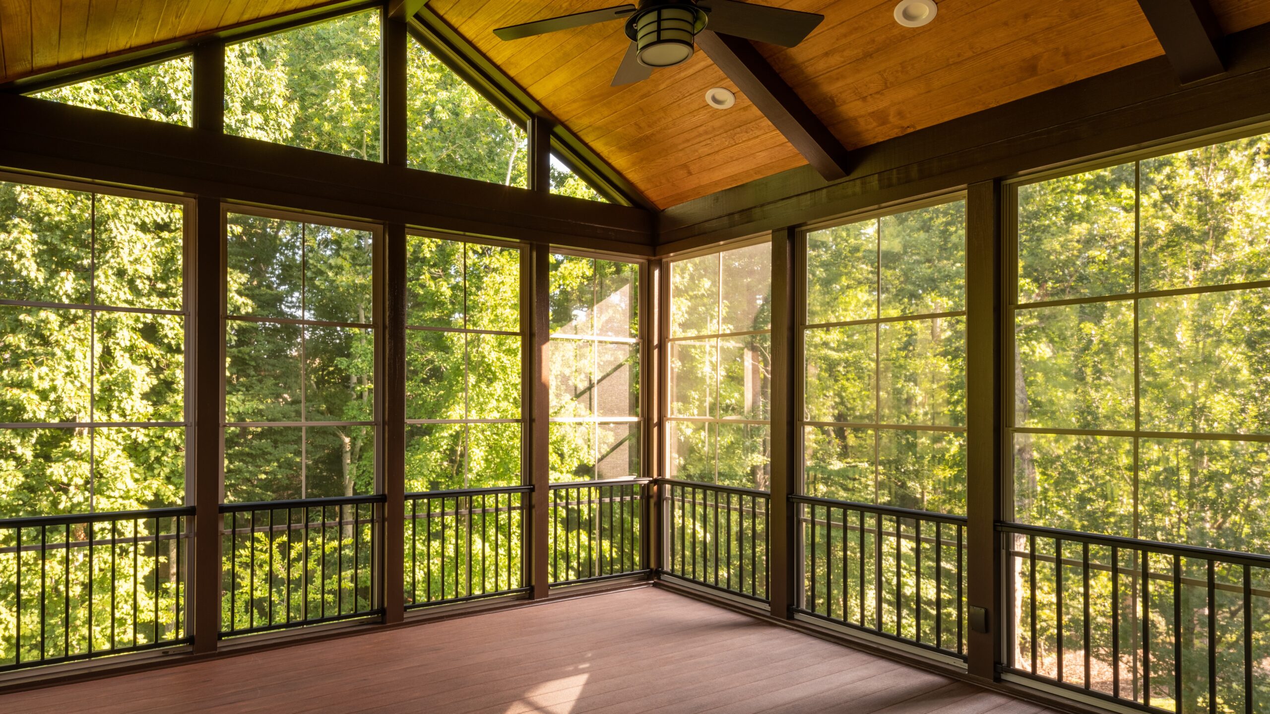 A sunroom with wooden flooring, glass walls, and a ceiling fan