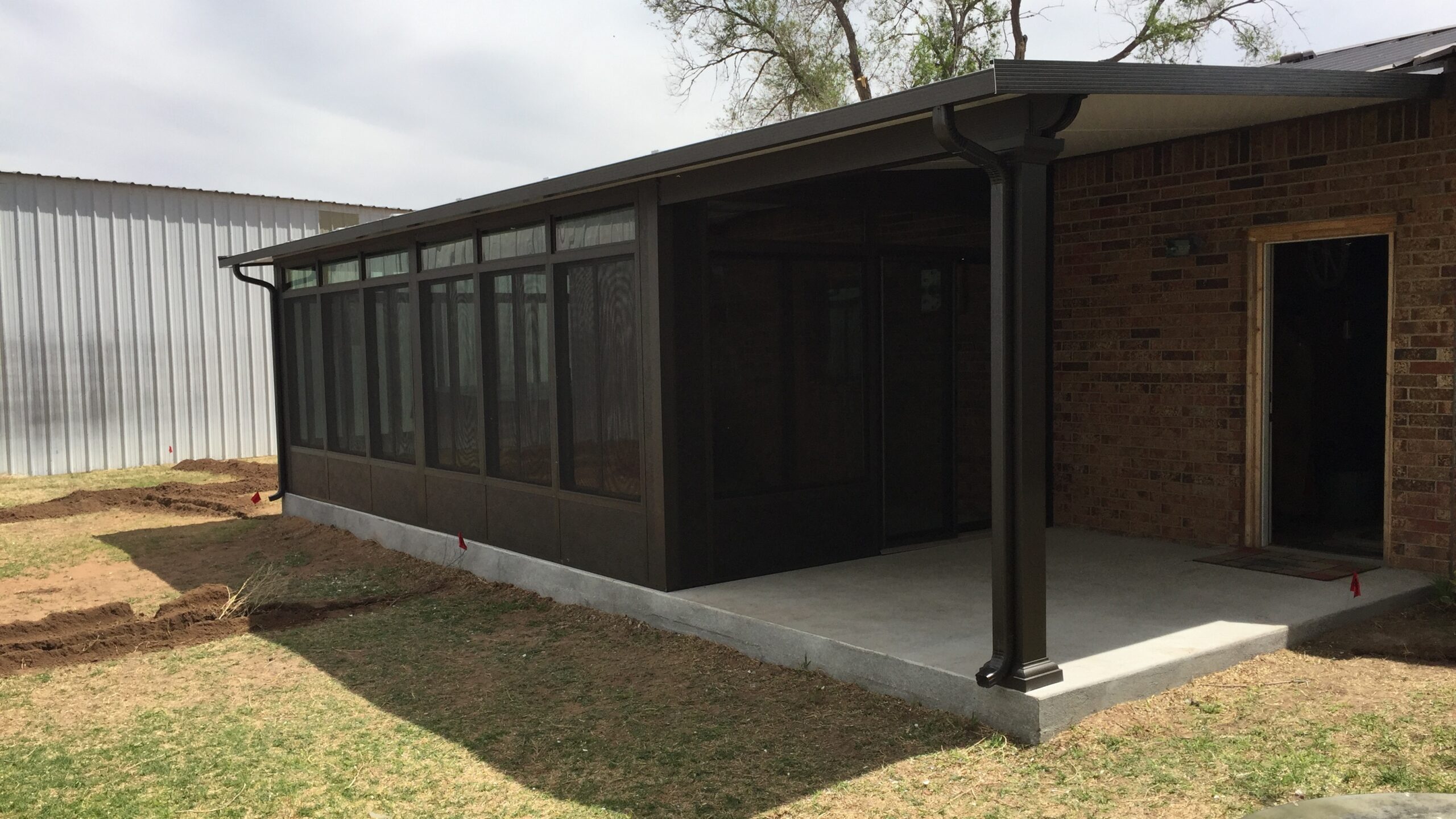 A black-framed TEMO sunroom installed next to a patio with a patio cover