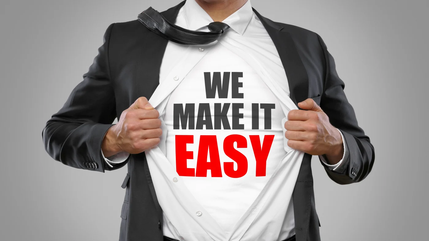 A man wearing a suit is seen from torso to neck. He pulls open his shirt and reveals a T-shirt that reads, “We make it easy.”