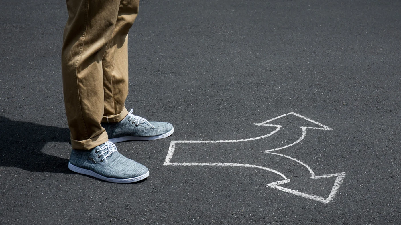 Person standing beside a hand-drawn arrow on pavement that branches into multiple directions, symbolizing thoughtful decision-making and choosing the right path.